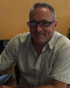 A man with glasses sitting in front of a wall.