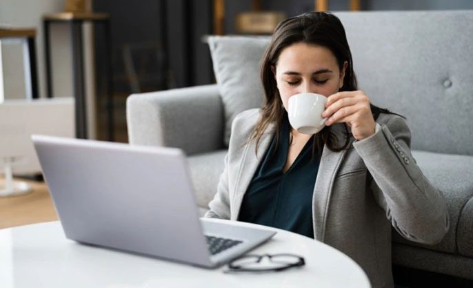 A woman drinking coffee while sitting at her laptop.