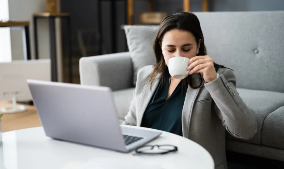 A woman drinking coffee while sitting at her laptop.